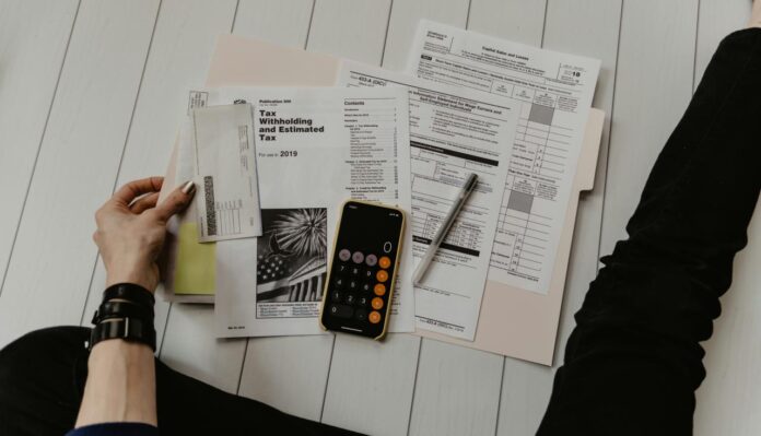 orang yang memegang kertas di dekat pena dan kalkulator