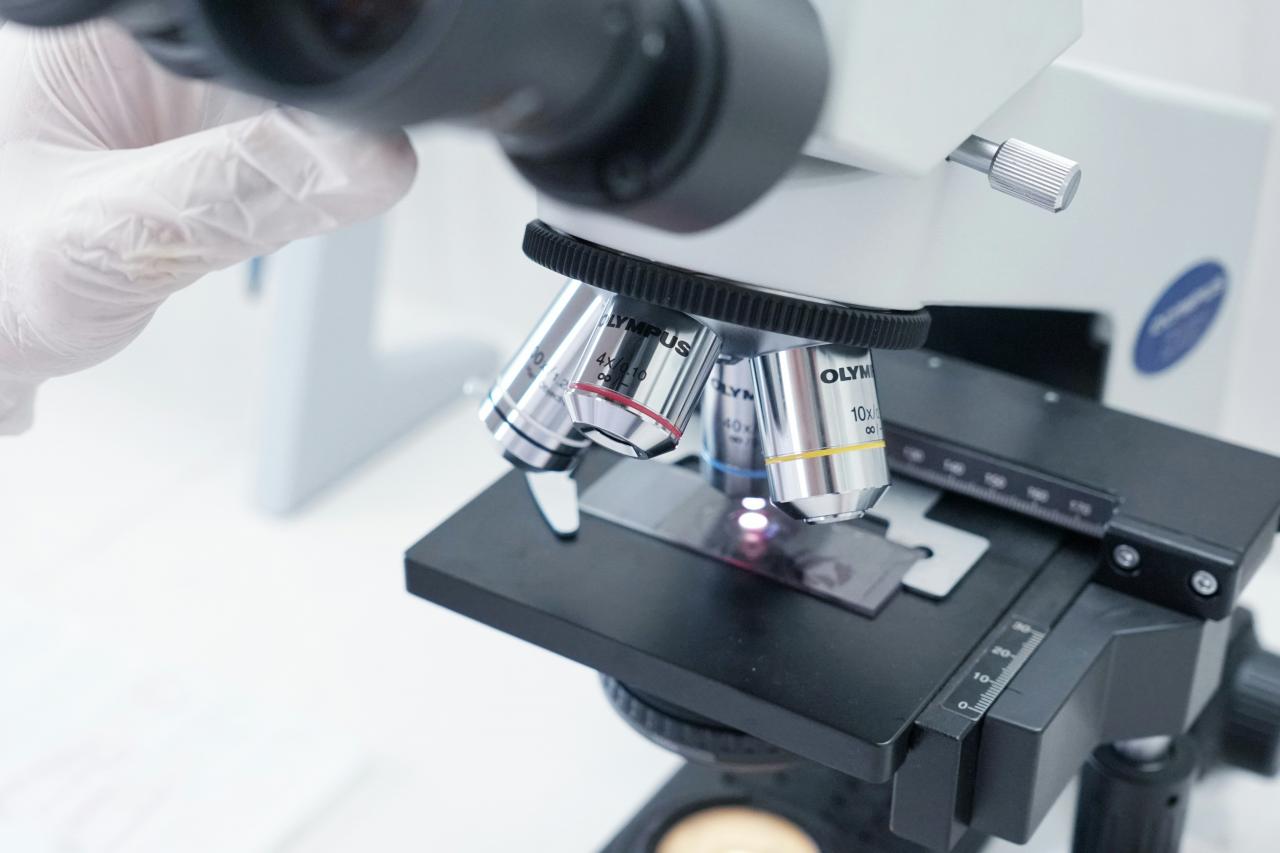 Seseorang dengan sarung tangan putih sedang melihat melalui mikroskop