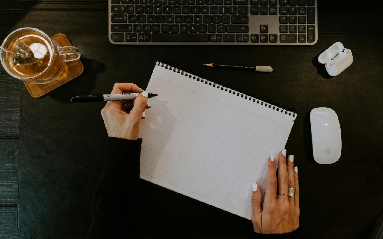 seseorang yang menulis di buku catatan di samping keyboard